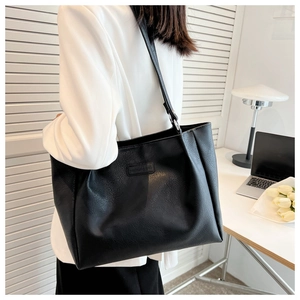 Detail view of a large black leather tote bag in a minimalist office setting with laptop
