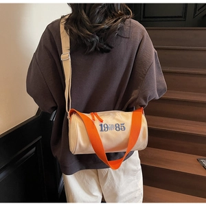 Détail du sac cylindrique en toile montrant la broderie bleue et la sangle contrastée