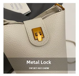 Detailaufnahme des goldenen Metallschlosses auf der cremeweißen Lederhandtasche
