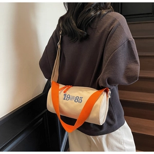 Détail du sac cylindre en toile avec bandoulière en nylon orange vif et broderie bleue
