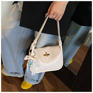 Close-up of off-white lychee leather shoulder bag featuring a gold twist lock and lace bow