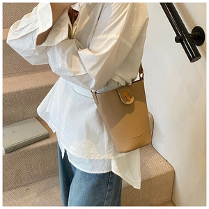 Detail einer beigen Bucket Bag aus Leder mit goldener Schließe und Logo am Modell