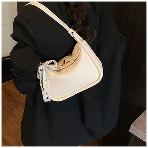 Detail of beige lychee leather crossbody bag with lace bow and pearl charm on a model