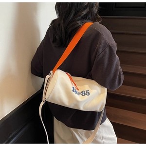 Détail de profil du sac cylindre en toile beige avec bandoulière orange contrastante