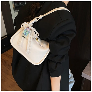 Detail showing white leather shoulder bag with lace bow and cartoon pendant charm