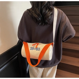 Détail d'un sac polochon en toile avec sangle orange porté par un mannequin sur escalier