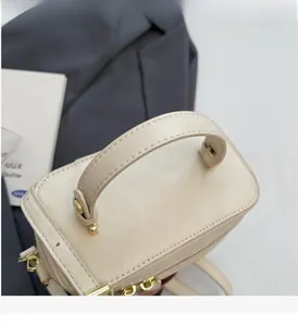 Détail du sac boîte crème montrant la texture du cuir et les ferrures dorées