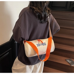 Détail du sac cylindrique en toile blanche avec bandoulière orange porté par un mannequin