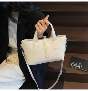 Close-up of cream glossy patent leather handbag with dual handles and slim shoulder strap