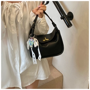 Detail of black pebbled leather handbag with golden twist lock and pearl lace charm