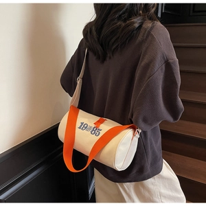 Détail du sac baril en toile avec sangle orange et broderie bleue porté par le mannequin