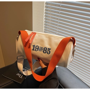 Détail du sac cylindre en toile avec broderie 1985 et bandoulière orange réglable