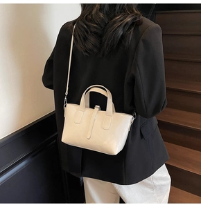 Side view of cream bucket bag with detachable strap shown on a model in a minimalist setting
