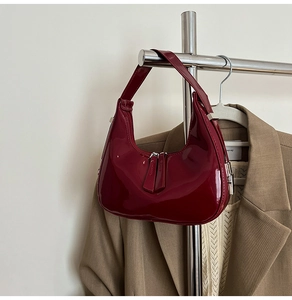 Détail d'un sac sous le bras en cuir verni rouge foncé avec fermetures éclair argentées