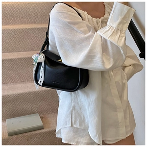 Close-up of black lychee leather shoulder bag with gold twist lock and lace bow charm