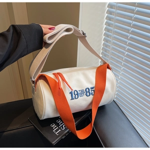 Gros plan détaillé d'un sac cylindre en toile avec poignées orange et broderie bleue