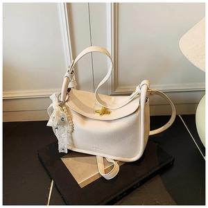Detail of white lychee leather bag featuring a gold twist lock and pearl lace charm