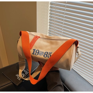Détail du sac cylindrique en toile avec broderie 1985 et bandoulière orange, style décontracté