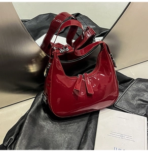 Détail du sac en cuir verni bordeaux avec zips argentés sur une surface texturée noire