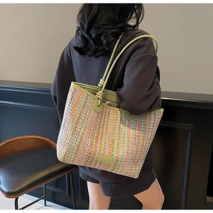Detailed close-up of colorful straw woven tote bag featuring green leather handle and brand tag