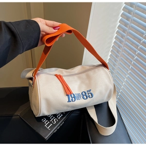 Détail du sac cylindrique en toile montrant la broderie bleue 1985 et la bandoulière
