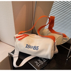 Détail du sac cylindre en toile avec broderie bleue et bandoulière orange vif