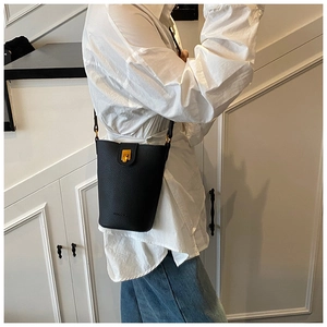 Detailansicht einer schwarzen Eimer-Tasche aus Leder mit goldenem Verschluss am Model