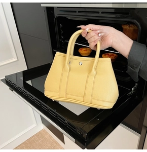 Detail der gelben Eimer-Tasche aus genarbtem Leder mit runder Schnalle und stabilen Griffen