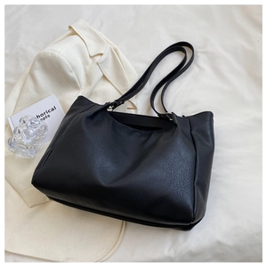 Detail of the black leather tote bag showing fine texture on a white blazer backdrop