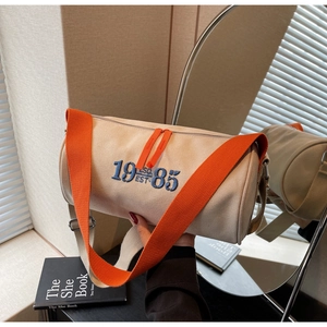 Détail du sac cylindre en toile beige avec broderie 1985 et bandoulière orange vive