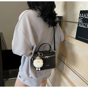 Chic black box crossbody bag with top handle and plush lamb charm shown on a model