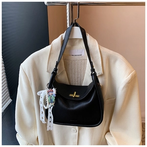Detail of black lychee leather shoulder bag with golden clasp and cute doll pendant