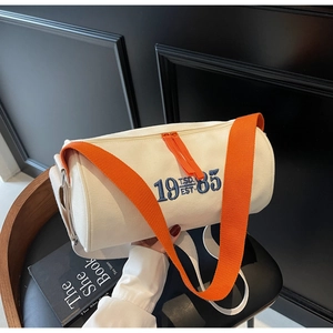Détail du sac cylindrique en toile blanche avec bandoulière orange et broderie