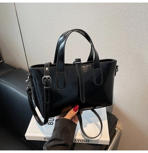 Detail of black glossy leather handbag with silver hardware and adjustable strap