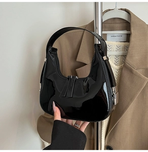 Détail d'un sac demi-lune en cuir verni noir avec boucle métallique argentée latérale