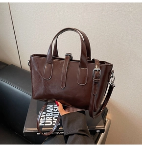 Close-up of polished dark brown bucket bag with shiny oil-wax texture and metal buckle
