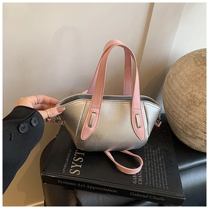 Detail view of silver pillow bag with pink handle and detachable shoulder strap on book