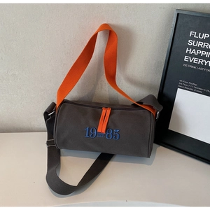 Détail du sac cylindre en toile avec broderie bleue et bandoulière orange vif