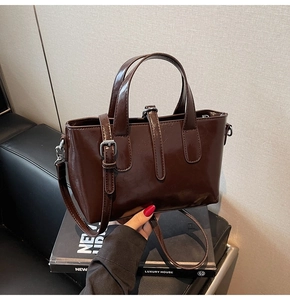Detail of dark brown patent leather tote bag with silver buckle and adjustable shoulder strap
