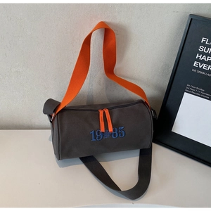 Détail du sac cylindrique en toile grise avec sangle orange et broderie 1985