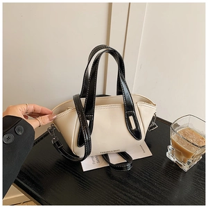 Detail of contrast stitching on beige and black leather pillow bag with metal hardware