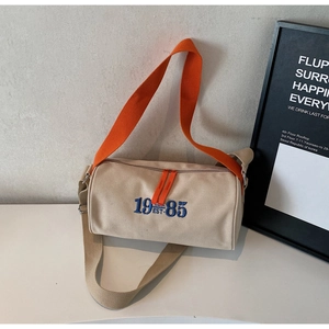 Détail du sac cylindre en toile avec broderie 1985 bleue et bandoulière orange