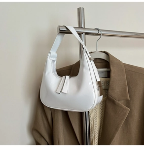 Détail d'un sac demi-lune blanc brillant avec finitions argentées sur tenue élégante