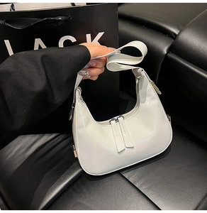 Détail du sac croissant en cuir verni blanc avec double zip et accents argentés