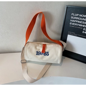 Détail du sac cylindre en toile avec broderie 1985 et fermetures éclair orange vif