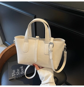 Close-up of white leather tote bag with metal buckle on a dark chair setting
