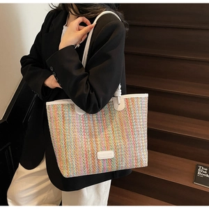 Colorful striped woven tote bag with white leather handles carried by a model outdoors