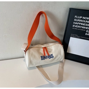Détail du sac polochon en toile avec broderie bleue et poignées orange contrastées