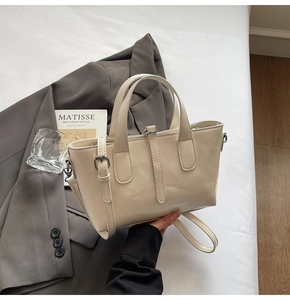 Detail of elegant cream faux leather handbag with decorative straps on minimalist background