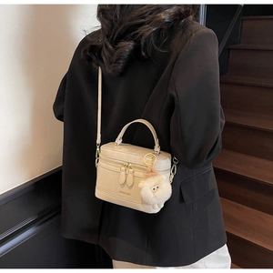 Dettaglio borsa a tracolla beige a scatola con un simpatico ciondolo a forma di pecora bianca